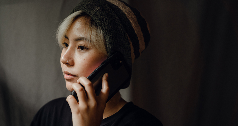 Stock photo of a somber teen talking on the phone in a dimly lit room. From Ketut Subiyanto on Pexels.