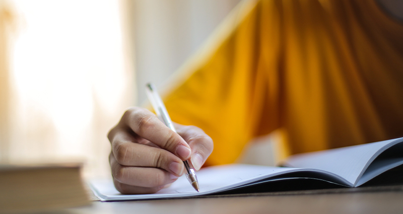 Stock photo of a person writing in a notebook. From Andrea Piacquadio on Pexels.