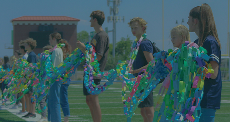 Photo of American Leadership Academy students holding a paper Chain of Hope across a football field.